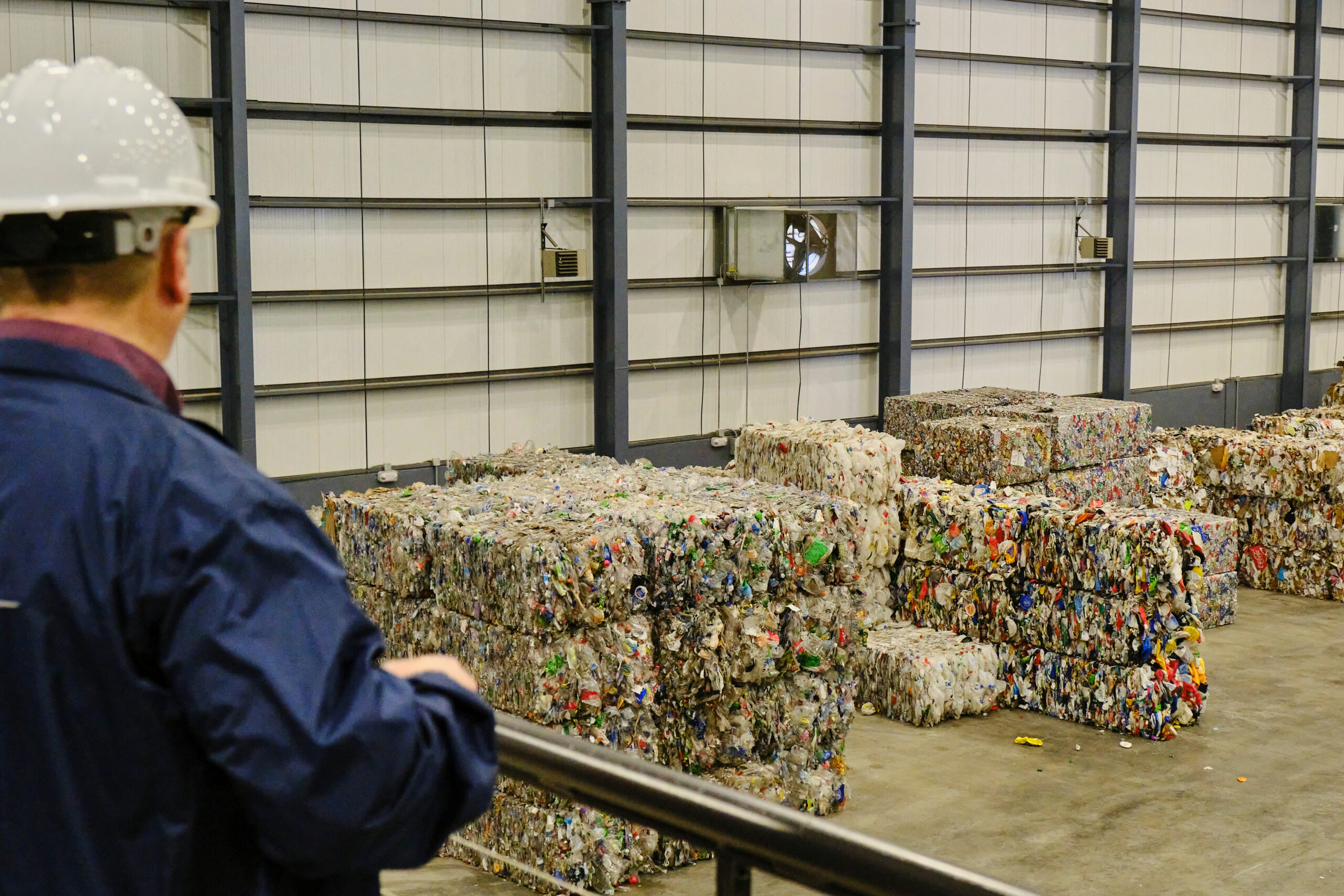A man in a hard hat looks out at bales of sorted materials ready to be recycled.